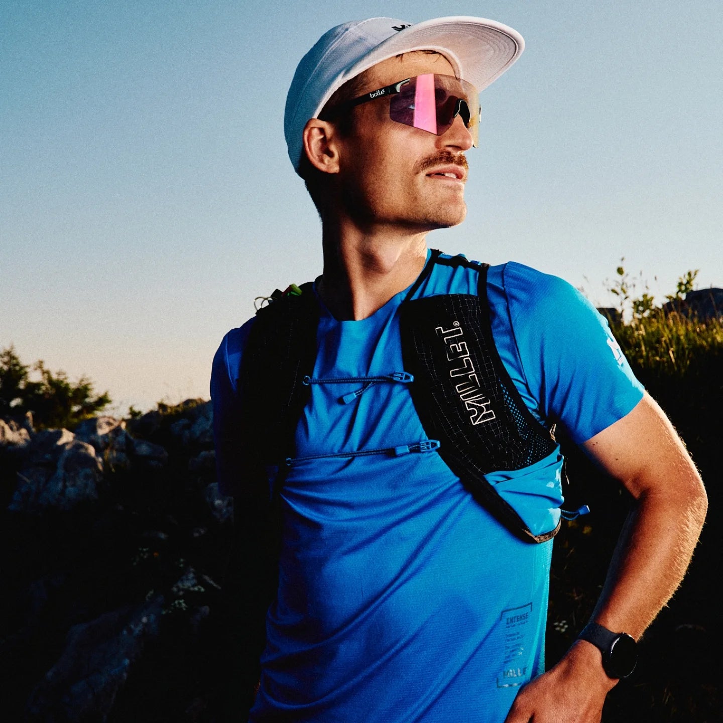 Man in blue athletic shirt and white cap with bolle sunglasses outdoors