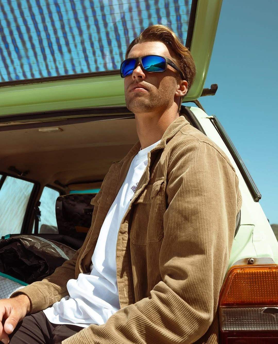 Man wearing maui Jim sunglasses sitting in an open-top vehicle with a clear blue sky.