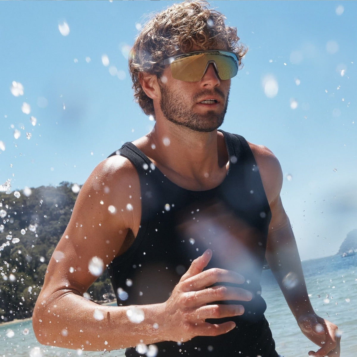 A man running on a beach wearing reflective gold-tinted maui jim sunglasses,