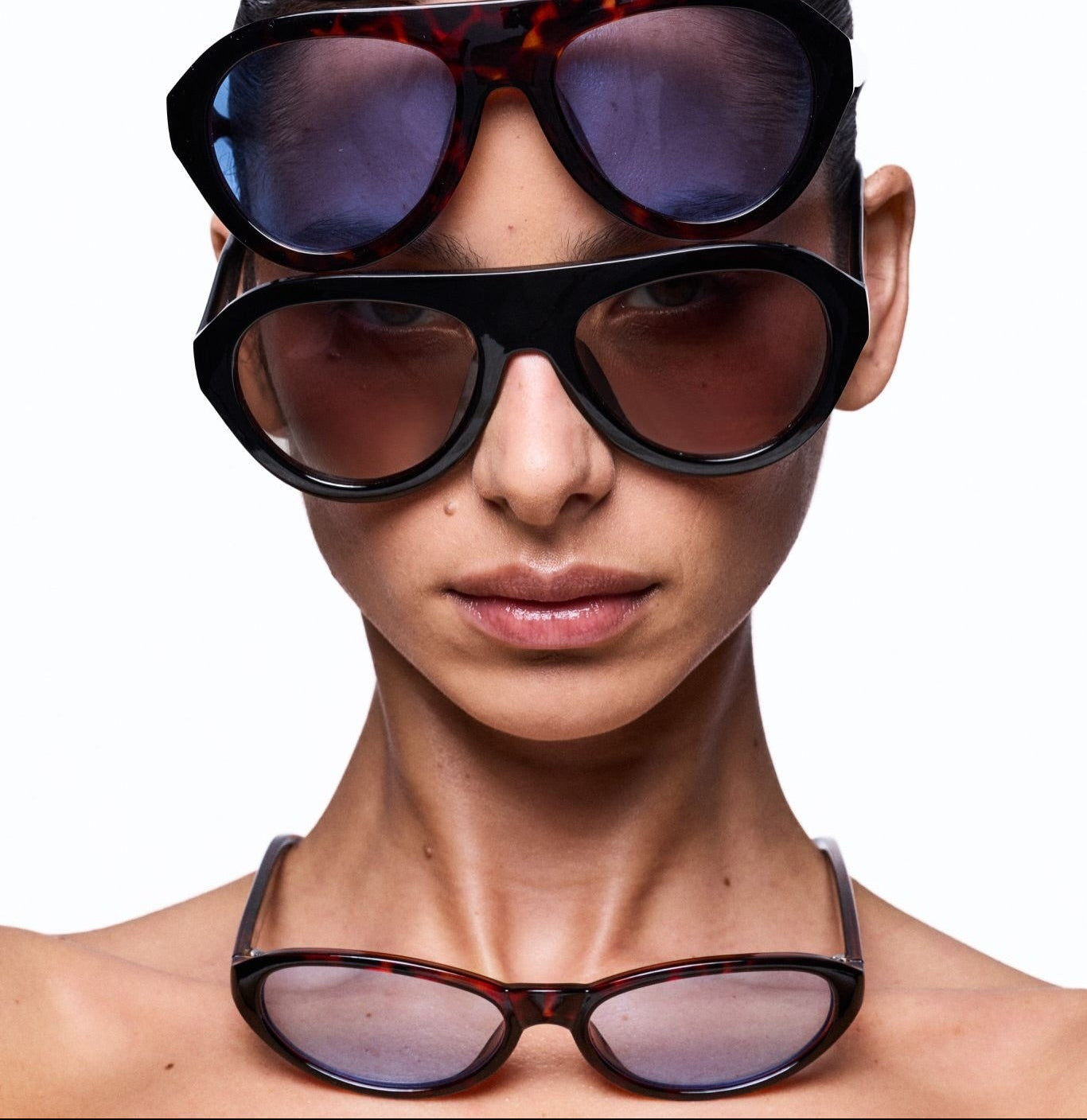 Woman wearing multiple pairs of OTRA sunglasses stacked on her head against a white background