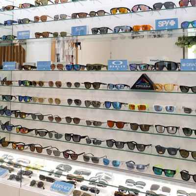 Display of sunglasses on shelves with various brands visible