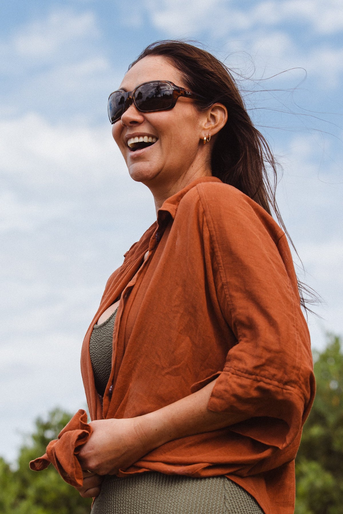 Woman wearing sunglasses and an orange shirt outdoors with a blue sky background
